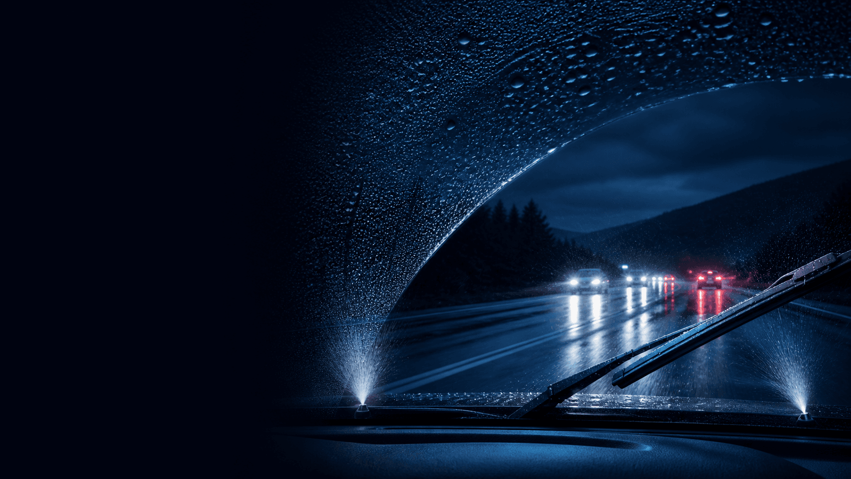 Rainy vehicle windscreen with washer spray, active wiper blades and clear wet-road visibility